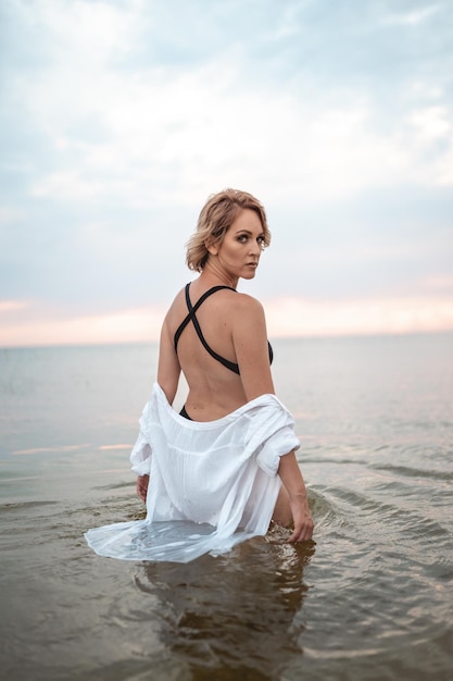 a girl in a black swimsuit and a white shirt is standing in the sea