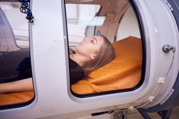 A girl in a black T-shirt lies in a hyperbaric chamber, oxygen therapy