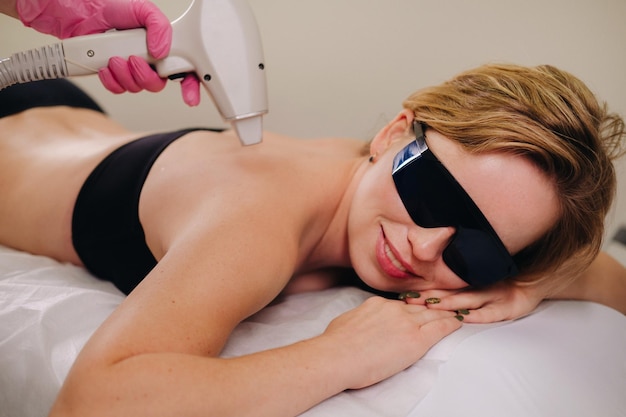 A girl in black underwear does laser hair removal on her back in the salon