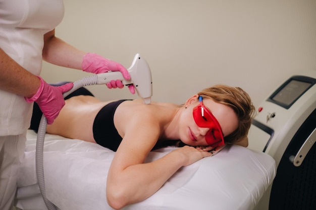 A girl in black underwear does laser hair removal on her back in the salon