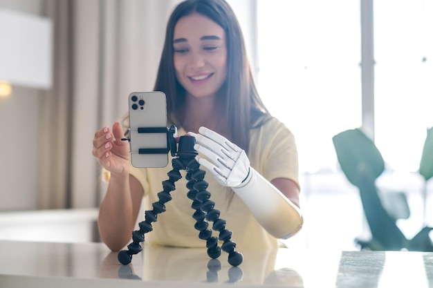 Girl blogger with bionic arm using phone live streaming social media at home woman with disability prosthetic limb working online remotely from home using artificial prosthetic limb