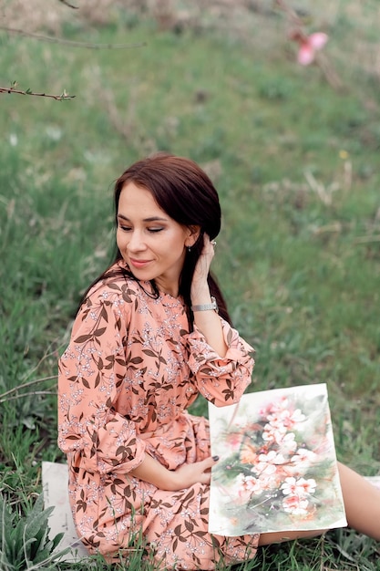 A girl in a blooming peach orchard is resting under a tree sitting and drawing