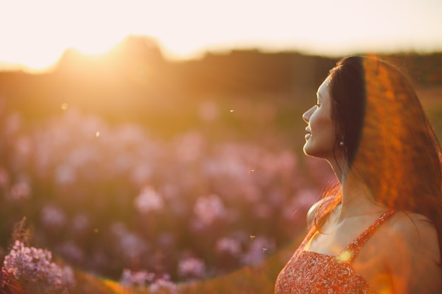 Girl on blooming Sally flower field at sunset. Lilac flowers and woman. Soft selective focus with sunflare.