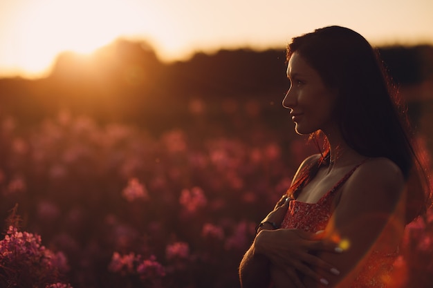 Girl on blooming Sally flower field at sunset. Lilac flowers and woman.