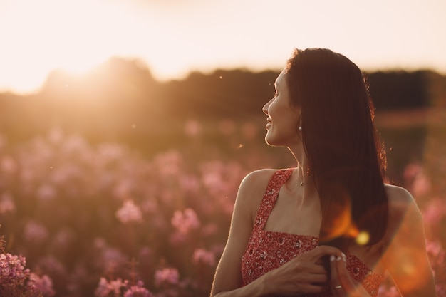 Girl on blooming Sally flower field at sunset. Lilac flowers and woman.