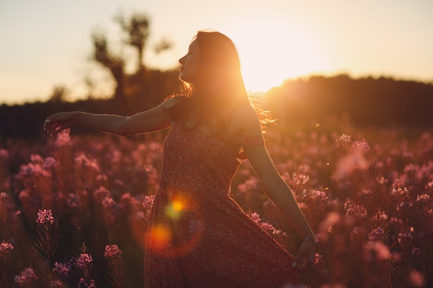 Girl on blooming Sally flower field at sunset. Lilac flowers and woman.