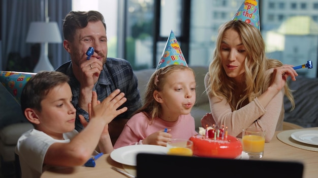 Girl blowing candles on cake with parents Family celebrating birthday online