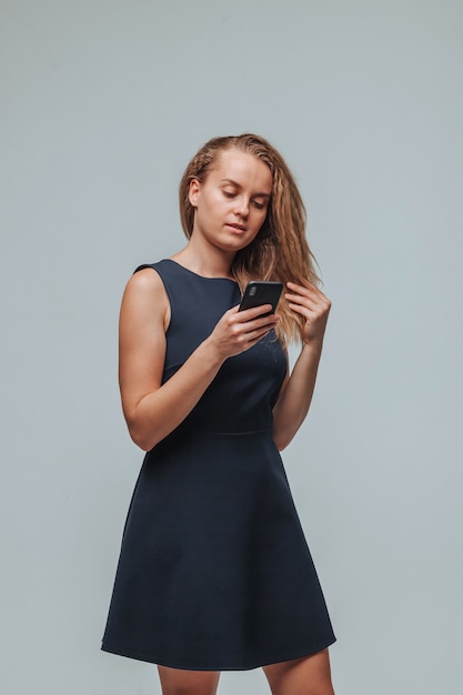 A girl in a blue dress is typing a message in the phone on a gray background