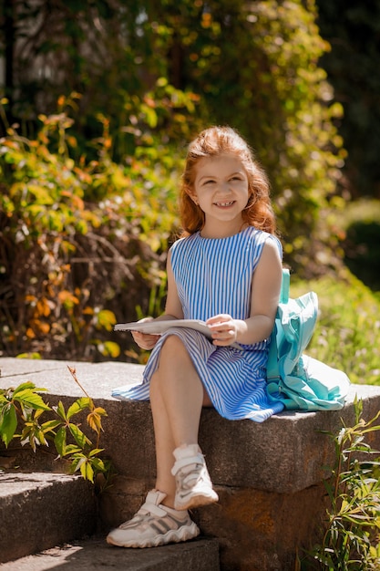 A girl in a blue dress sitting and holding a book