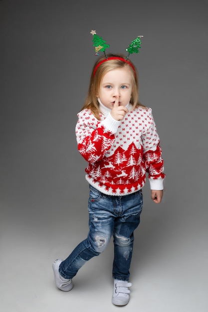 Girl in blue ripped jeans and red and white sweater pressing the finger to her lips.