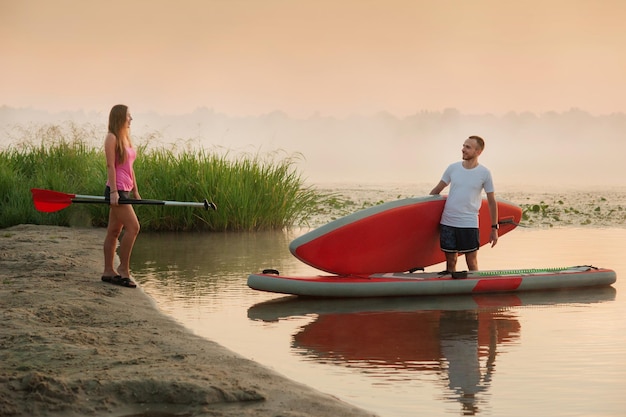 A girl and a boy are preparing to swim on a standup paddle board active recreation of lovers tourism on the water