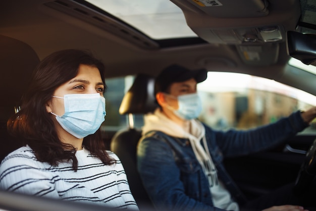 A girl and a boy driving in a car during coronavirus quarantine wearing medical masks