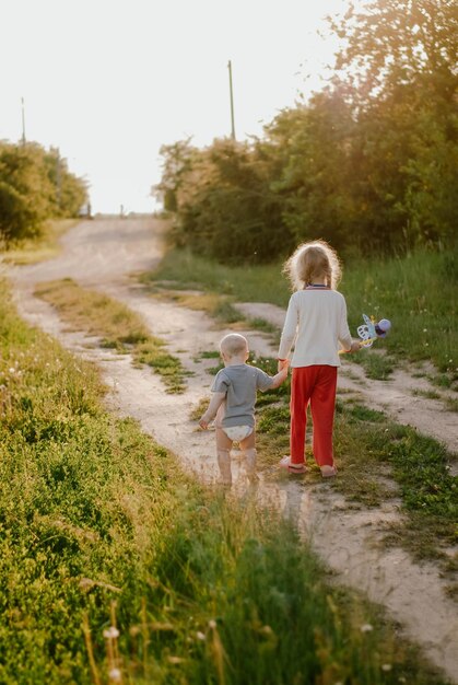 a girl and a boy walk by the hand brother and sister children summer evening sunlight