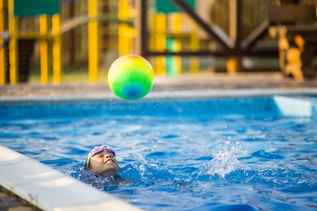 A girl in a bright bathing suit swims with an inflatable ball in a pool with clear water on a summer evening