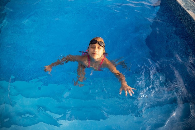 A girl in a bright swimsuit with swimming goggles dives into a pool with clear transparent water