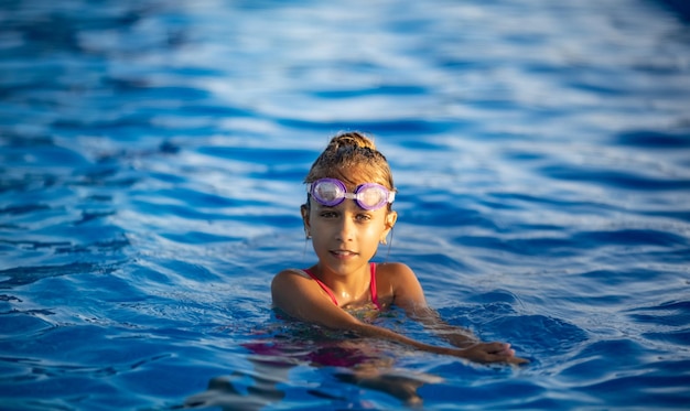 A girl in a bright swimsuit with swimming goggles dives into a pool with clear transparent water