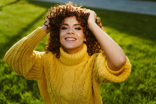 Photo a girl in a bright yellow sweater shaggy her brown curly hair against a background of green grass