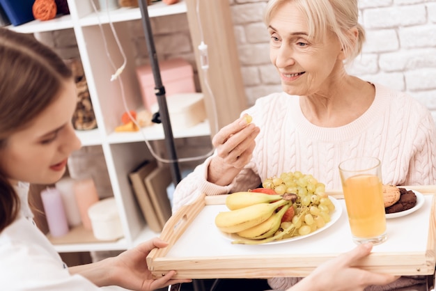 Girl brings breakfast on tray. Woman is eating.