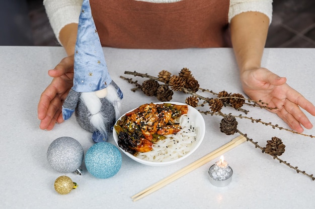 Girl in a brown apron Plate with rice noodles and chicken Festive decoration Dark home kitchen background Christmas concept