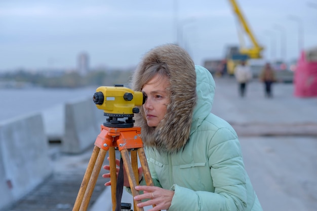 The girl the builder in warm clothes looks in a theodolite.