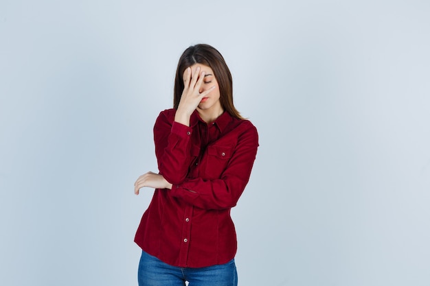 girl in burgundy shirt holding hand on face and looking fatigued.