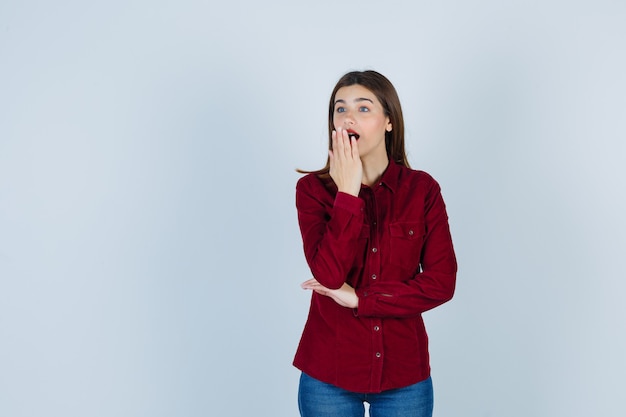 girl in burgundy shirt looking away with hand on mouth and looking surprised