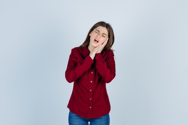 girl in burgundy shirt suffering from terrible toothache and looking bothered.