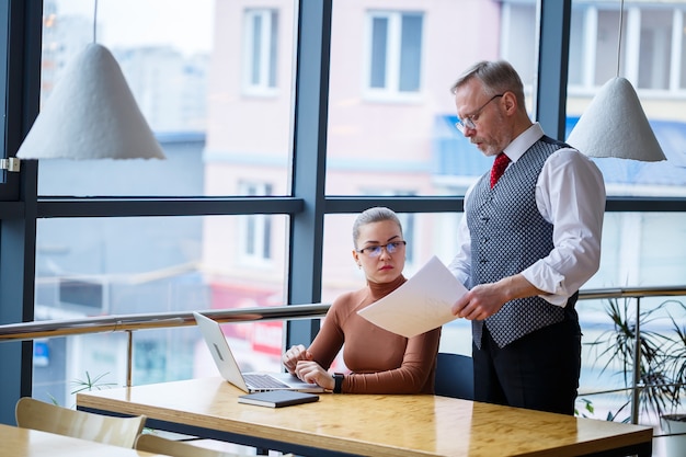 Girl business lady sitting at a wooden table with a laptop and working teacher boss mentor indicates her mistakes. School of a new business development concept.