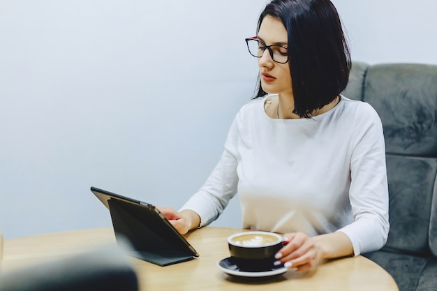 Girl in cafe drinks coffee and works on tablet