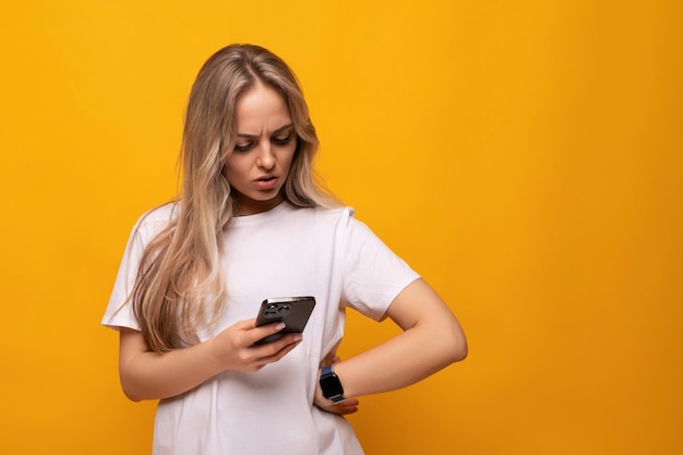 The girl carefully scrolls the application in the phone on a yellow background