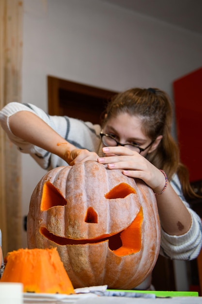 A girl carving big orange pumpkin into jackolantern for Halloween holiday decoration at kitchen Decoration for party