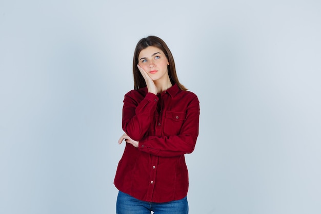 girl in casual shirt leaning cheek on palm, looking up and looking thoughtful