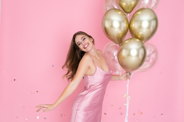 Girl celebrates new year or happy birthday party holds air balloons in shiny dress throwing confetti