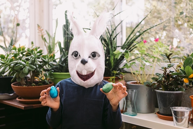 Girl celebrating Easter with a rabbit mask and some chocolate eggs in a glassedin area surrounded by plants Easter celebration and costume concept