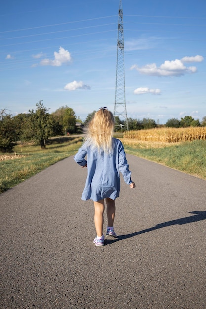 Girl child in a dress running with her back along the road in the field