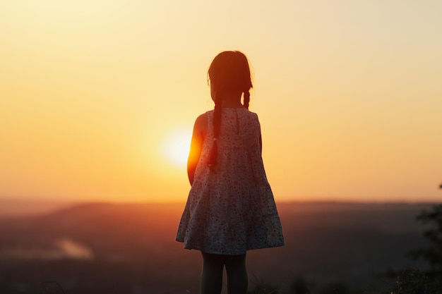 Girl child standing on the hill and watching the sunset