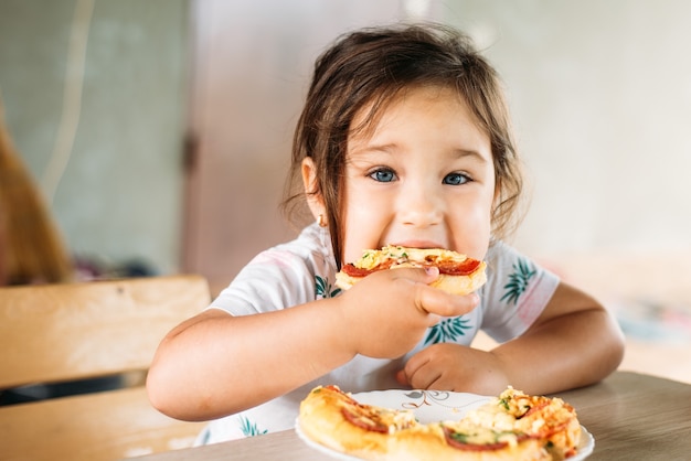 A girl a child on the street eats a mini pizza very appetizing