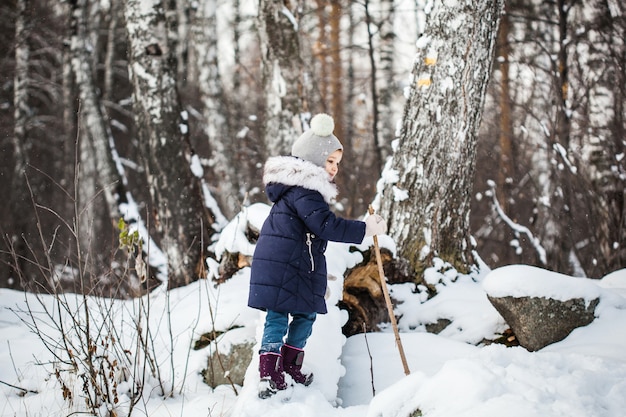 Girl child walking in the winter forest in a blue jacket and gray hat