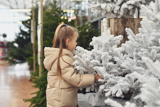 A girl and a christmas artificial trees for sale on a shop