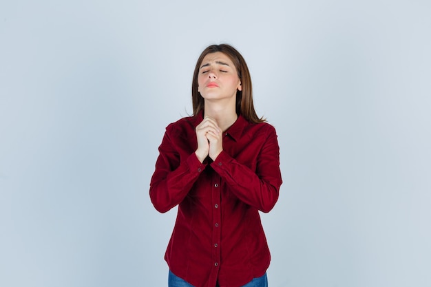 girl clasping hands in praying gesture in burgundy shirt and looking hopeful.