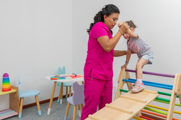 Girl climbs wooden game in pediatrician doctor's office while they help her to climb