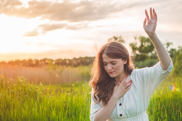 Girl closed her eyes, praying in a field during beautiful sunset