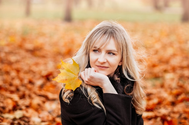 Girl collects yellow leaves in autumn. Young woman enjoying autumn weather.