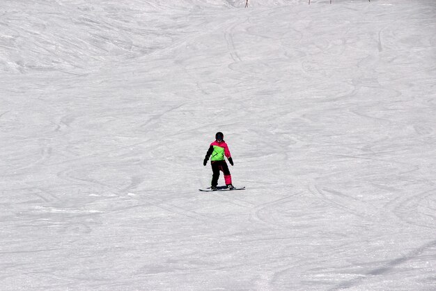 Girl in a colorful suit is on a snowboard rides with mountains