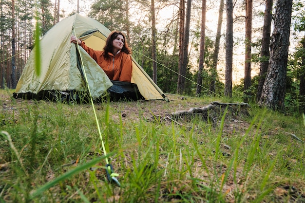 The girl comes out of the tent after sleeping. Travel outside the city in the woods. Camping.