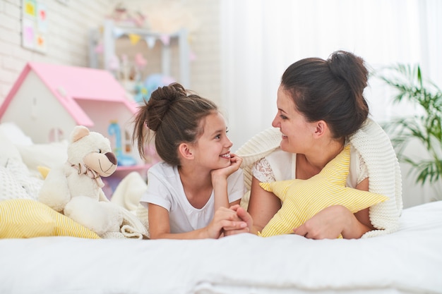 Girl congratulates mother. Mom and daughter smile and hug while lying on bed.