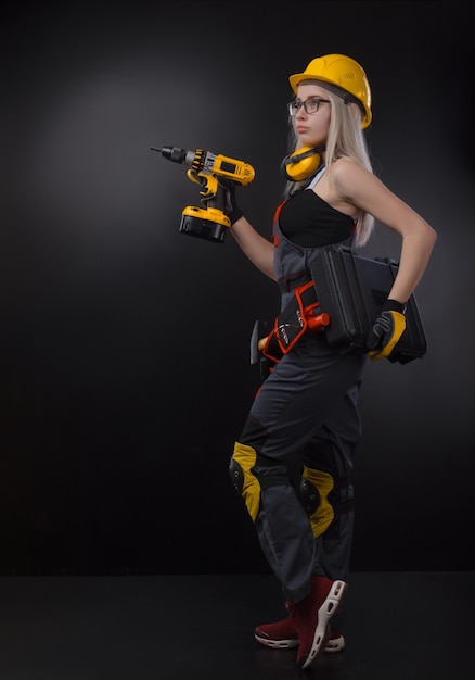 The girl in construction clothes and protective equipment posing with a screwdriver