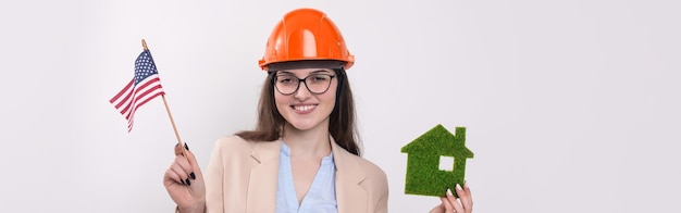 A girl in a construction helmet and an American flag holds a green eco house