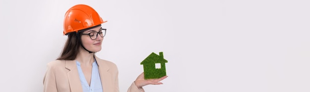 A girl in a construction helmet holds a green house The concept of ecological clean housing