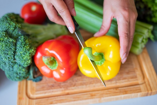 girl cook in the kitchen cuts red paprika with vegetables with a knife